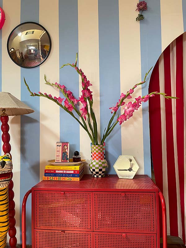 The striped wallpaper and curtain are perfectly paired with a chequered vase that exudes a maximalist vibe. (Image Credits: Ishita Sitwala) 