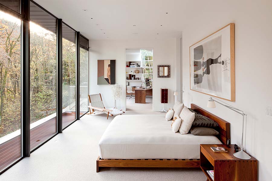 Floor-to-ceiling windows fill the bedroom with natural light, creating a seamless connection to the surrounding forest. (Image Credit: Jeremy Bittermann) 