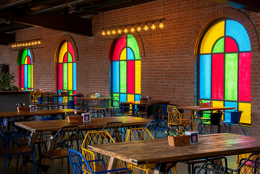 The bare bulb fixtures from Light and Living (Bengaluru) add a touch of rustic charm, while the furniture from Saumitra International (Jodhpur) looks cosy and inviting against the brick walls and stained glass windows. (Image Credits: The Bier Library) 