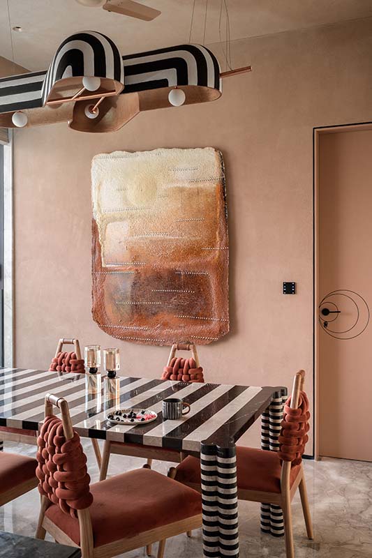 The dining area features artwork that adds to the warmth, paired with Veev chairs by Design By DHEX and a stripped lamp from Design By DH. (Image Credits: Wabi Sabi)